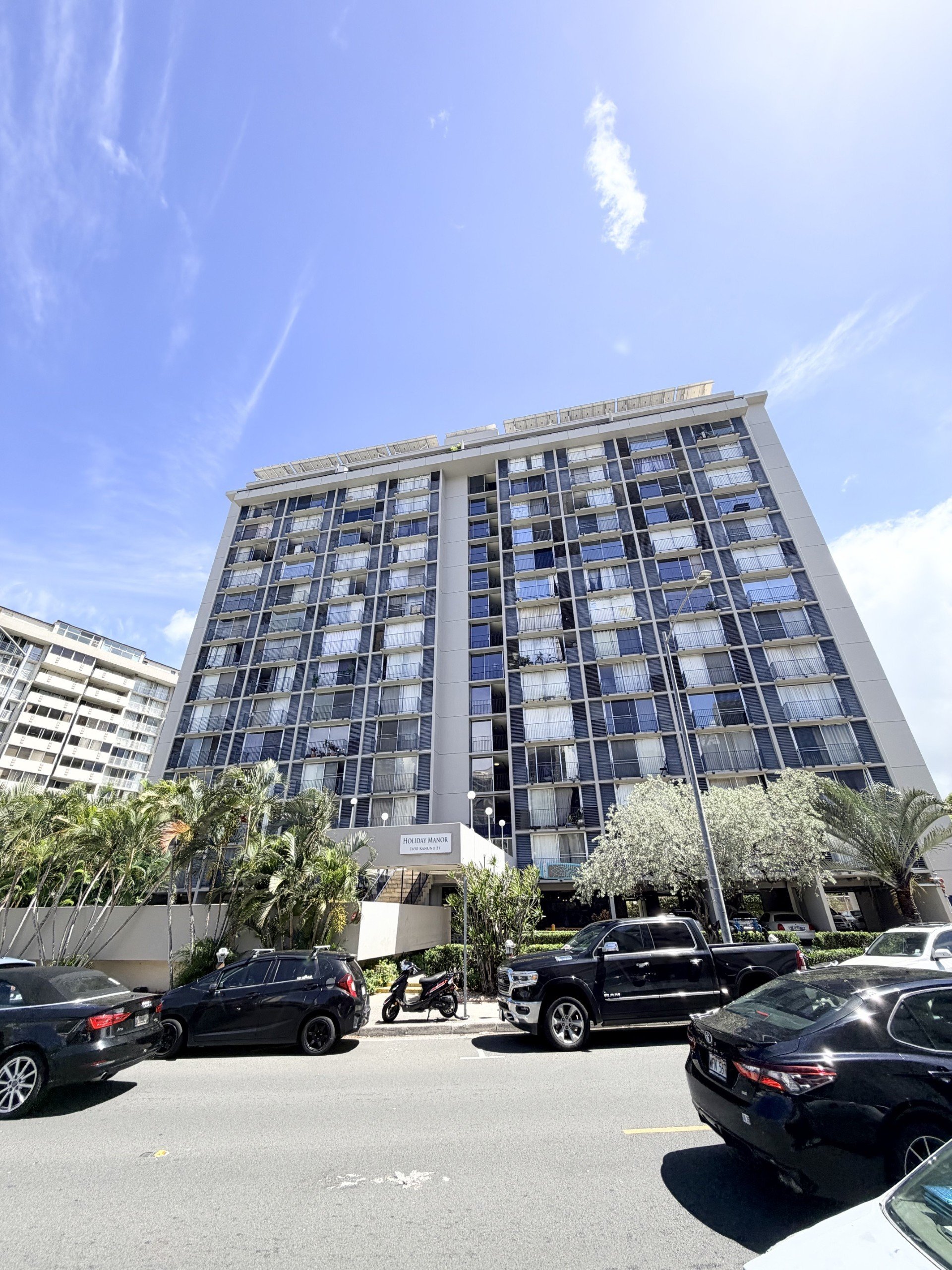 A tall building with many windows is surrounded by parked cars.
